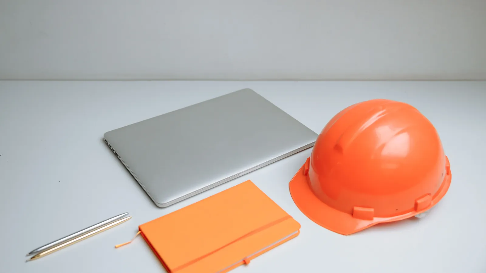 Orange hardhat beside a closed laptop and notebook