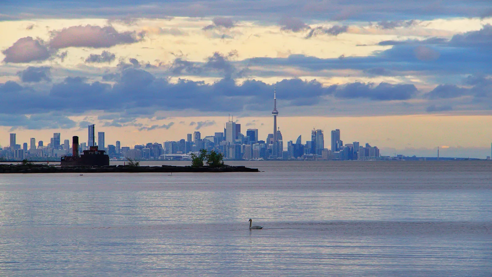 Distant city skyline across calm water beneath layered clouds