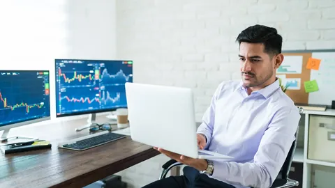 Trader at a desk with a laptop and two chart monitors