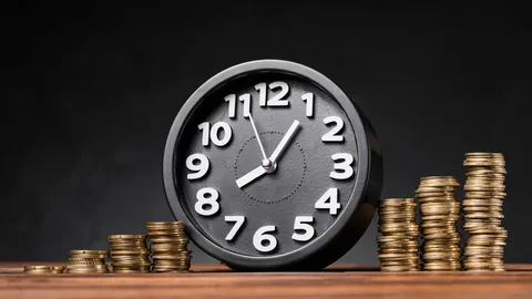 Alarm clock standing beside stacks of coins