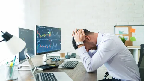 Stressed trader holding his head in front of chart monitors