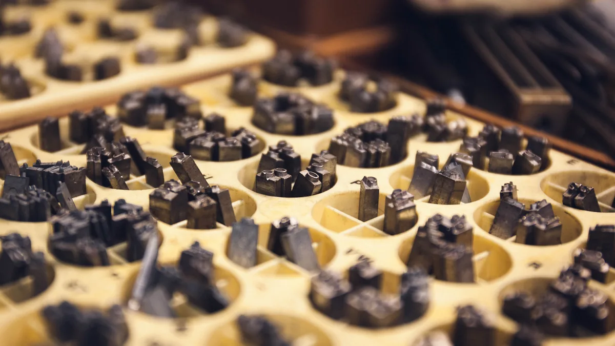 Metal letterpress type pieces sitting in a wooden printer's tray