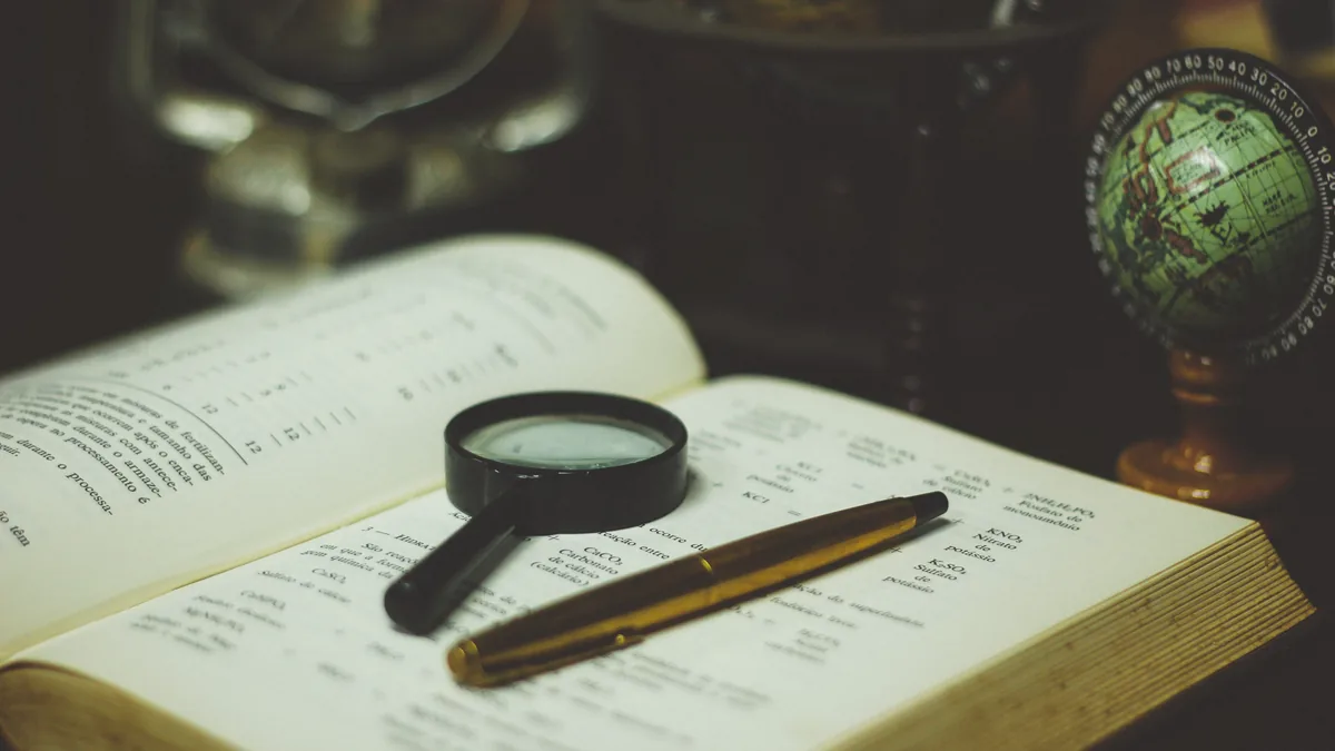 A magnifying glass and a pen resting on an open book beside small globes