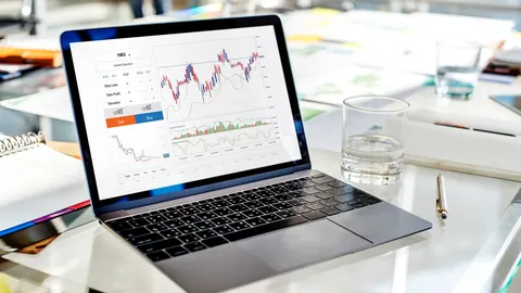 Laptop on a desk showing a trading platform with a candlestick chart