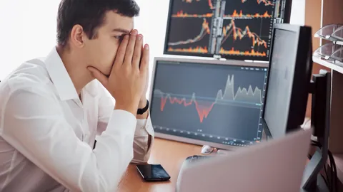 Worried trader covering his face in front of falling chart monitors