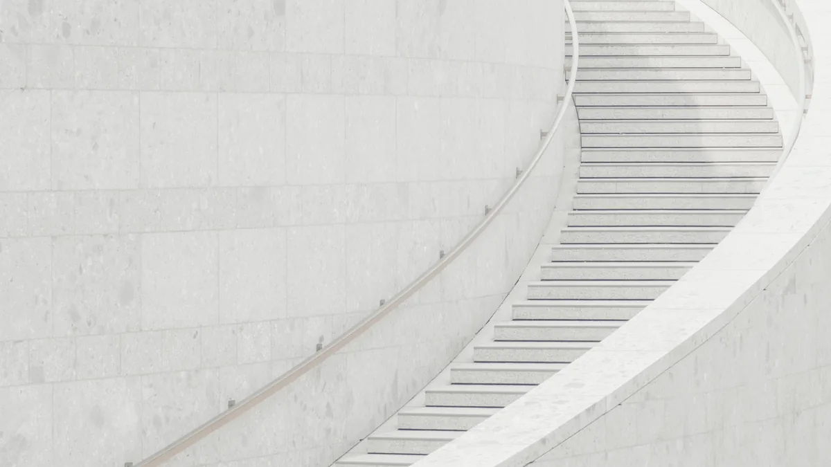 A curving white marble staircase climbing past a pale wall, one flight after another