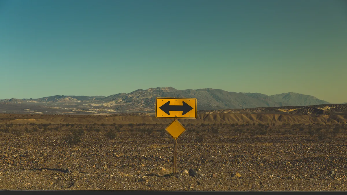 A yellow double-arrow road sign pointing both ways across a desert plain