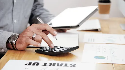 Person using a calculator beside a laptop and printed documents