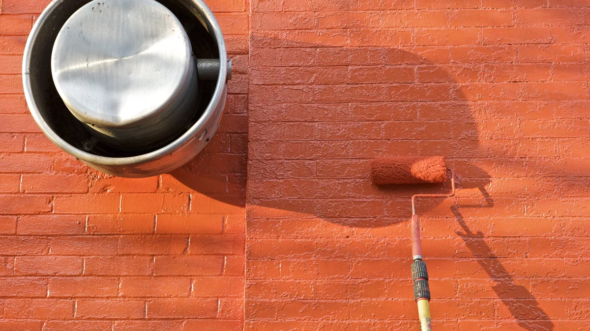 A paint roller giving a brick wall a fresh coat of orange paint