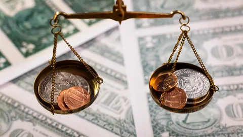 Brass balance scale with coins on each pan over dollar banknotes