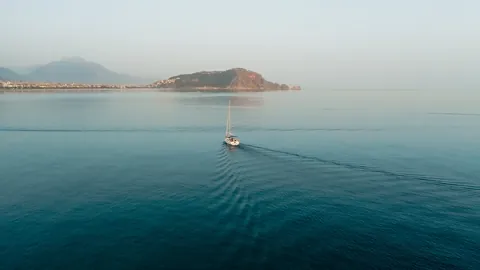 Sailing boat crossing calm water towards an island