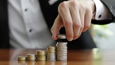 Hand placing a coin on the tallest of several coin stacks