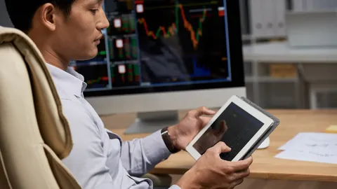 Trader reading a tablet in front of chart monitors