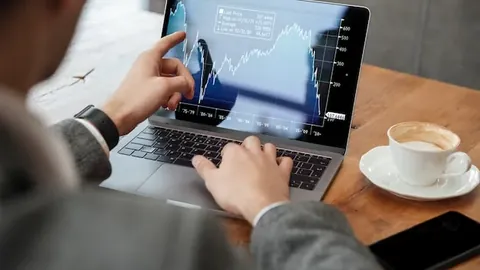 Cropped image of businessman sitting by the table in cafe and analyzing indicators on laptop computer